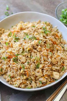 a white bowl filled with rice and veggies next to chopsticks on a table