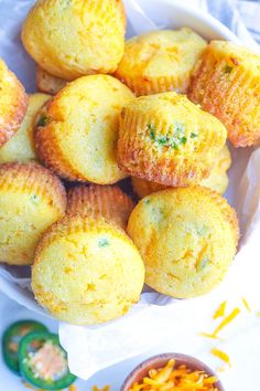 a bowl filled with yellow muffins next to a small bowl of shredded cheese