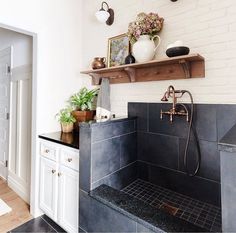 a bathroom with black and white tile, wooden shelves and potted plants on the wall