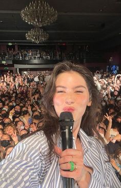 a woman standing in front of a crowd holding a microphone and making a funny face