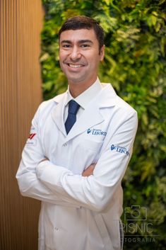 a man in a lab coat and tie standing with his arms crossed, smiling at the camera