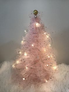 a pink christmas tree with white lights and some decorations on the top is sitting on a furry surface