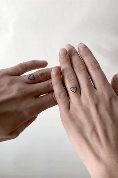 two hands touching each other with hearts tattooed on their fingers