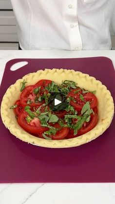 a person sitting at a table in front of a pie with tomatoes and herbs on it