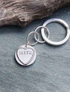 a heart shaped metal keychain with the word eeze on it sitting next to a piece of driftwood