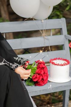 a woman sitting on a bench next to a white cake and red roses with sparklers