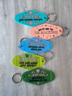 four keychains with sayings on them sitting on a wooden surface in different colors