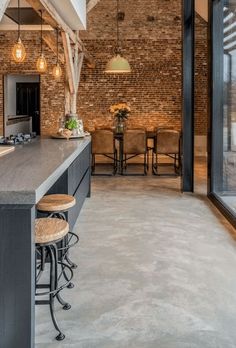 an open kitchen and dining area with exposed brick walls, floor to ceiling windows, and bar stools