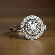 a diamond ring on a wooden table with diamonds around it and the center stone is surrounded by smaller round brilliant cut diamonds