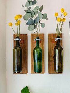 three green bottles with flowers in them are on the wall next to a planter