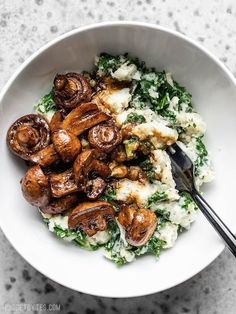 a white bowl filled with food on top of a marble counter next to a fork