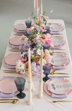 the table is set with pink and purple plates, silverware, candles, and floral centerpieces