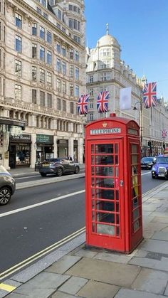 a red phone booth sitting on the side of a road next to tall buildings and cars