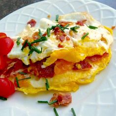 a white plate topped with an omelet covered in bacon and cheese next to tomatoes