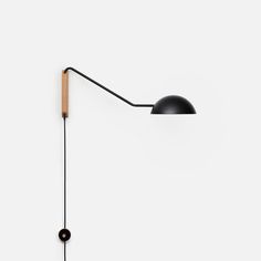 a black wall lamp with a wooden arm on a white wall next to a light bulb