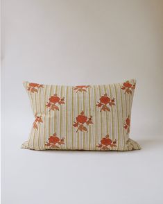 an orange and white striped pillow with red flowers on the front, against a beige background