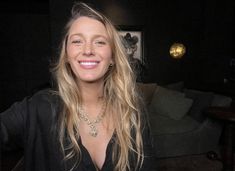 a woman with long blonde hair wearing a black shirt and gold necklace smiling at the camera