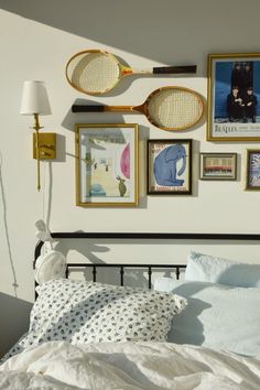 a bed with white sheets and pictures on the wall above it, along with tennis racquets