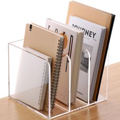 a clear acrylic desk organizer with spiral binders and notebooks in it