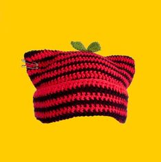 a red and black knitted hat with a green leaf on the top, against a yellow background