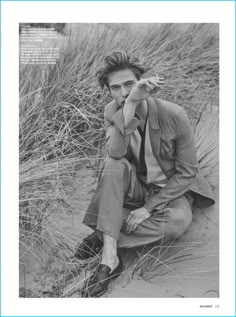 a black and white photo of a man in a suit sitting on the sand dunes