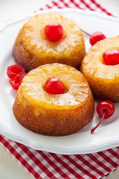 three pineapple upside down cakes on a white plate with cherries around the edges