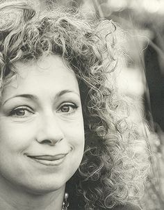 a black and white photo of a woman with long curly hair smiling at the camera