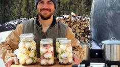 a man holding three jars filled with pickled onions on top of a wooden board