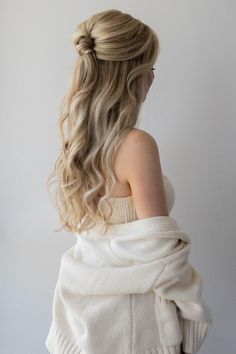 a woman with long blonde hair wearing a white sweater and holding her back to the camera