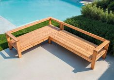 a wooden bench sitting on top of a cement floor next to a swimming pool and lush green grass