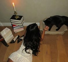 a woman laying on the floor next to a cat and a stack of books with a lit candle