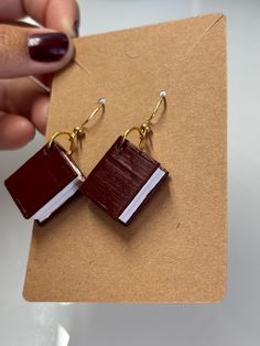 a pair of red and white book earrings on a brown piece of paper with gold earwires