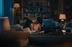 three people sitting on a couch in a living room looking at an electronic tablet computer