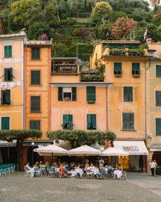 people are sitting at tables outside in front of buildings with green shutters and windows