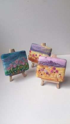 three miniature paintings on wooden easels sitting on a white surface, each painted with different colors