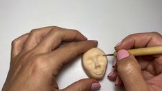 two hands are holding a pencil and an object with a face carved into the side