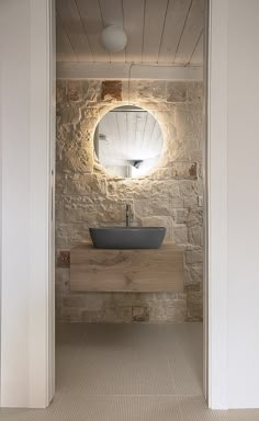 an open door leading to a bathroom with stone walls and a round mirror on the wall