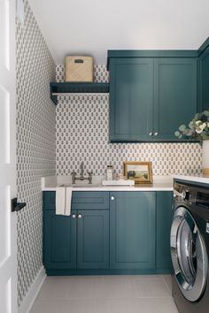 a washer and dryer in a small room with blue cabinetry, patterned wallpaper, and tile flooring