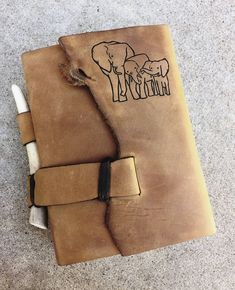 an elephant is drawn on the side of a brown leather book with two pencils in it