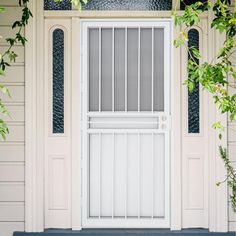 a white door and window on a house with green plants growing around the front porch