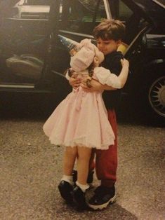 a young boy and girl hugging each other in front of a car