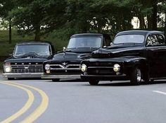 three classic cars are parked on the side of the road in front of some trees