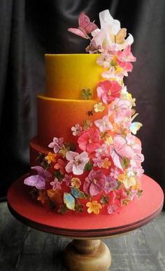 a multi - colored cake with flowers on top sits on a table in front of a window