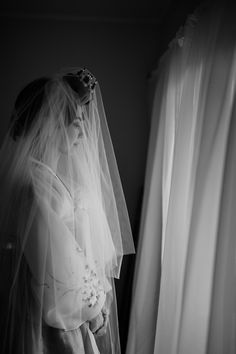 a woman in a wedding dress standing next to a window with her veil over her face