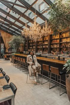 two people sitting at a bar with chandeliers hanging from the ceiling