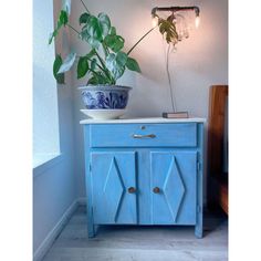 a potted plant sitting on top of a blue cabinet next to a light fixture