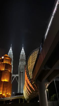 two tall buildings lit up at night with lights in the sky and below them are skyscrapers