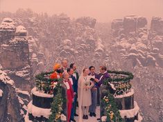 a group of people standing next to each other in front of snow covered mountains and trees