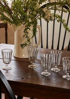 a wooden table topped with glasses next to a vase filled with flowers