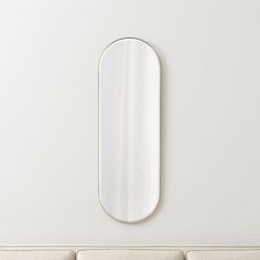 an oval mirror mounted on the wall above a couch in a room with white walls